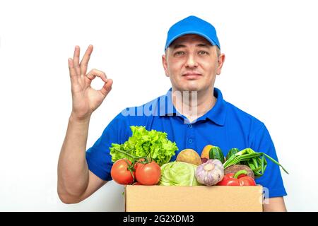 Cheerful delivery man of fresh vegetables in a blue uniform on a white background. Stock Photo