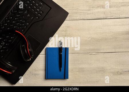 Laptop, notebook and headphones lie on a wooden table. There is a place on the right for an inscription Stock Photo