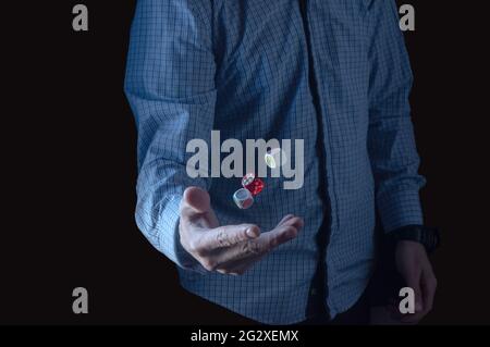 The man tosses the dice. Three cubes in the air. A man in a plaid shirt. Low key. Stock Photo