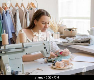 Happy female dressmaker or seamstress using cell phone at her workplace in atelier Stock Photo