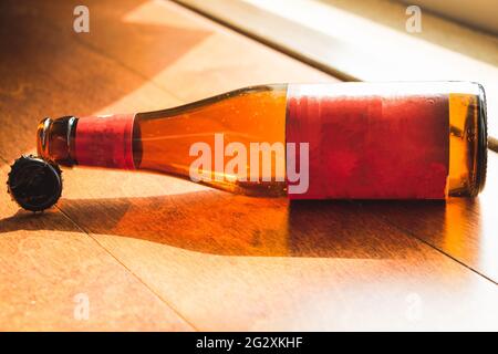 Shiny empty beer bottle lying down on wooden floor in natural light Stock Photo