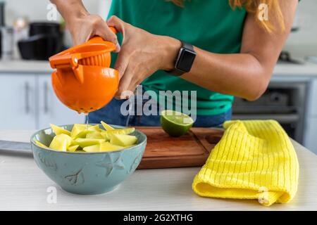 woman squeezing lemon over mango in a bowl in the kitchen Stock Photo