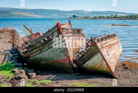 Beautiful seascape with three semi-destroyed wooden fishing boats left in the beach and the Sound of Mull in the background. Isle of Mull, Inner Hebri Stock Photo