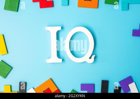 IQ text with colorful wood puzzle pieces, geometric shape block on blue background. Concept of intelligence quotient and logic thinking Stock Photo