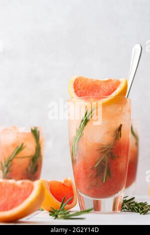 Cold refreshing grapefruit smoothie with rosemary and ice in glass close up, grapefruit wedges and rosemary sprigs on the table, home party Stock Photo