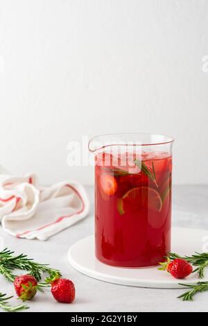 Fresh strawberry and lime drink with ice and rosemary in a jug close-up, summer refreshing lemonade Stock Photo