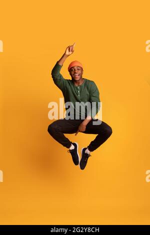 Check This. Cheerful Young Black Guy Pointing Up And Down While Jumping Stock Photo