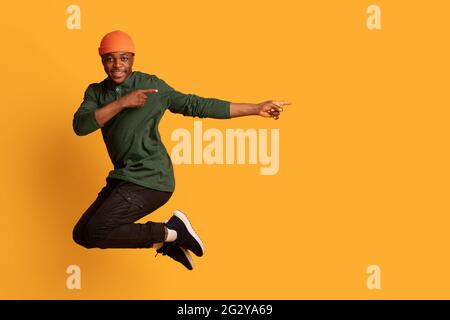 Look At This. Cherful african guy pointing aside while jumping in air Stock Photo