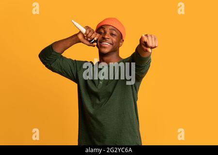 Joyful young black man singing with microphone and pointing at camera Stock Photo