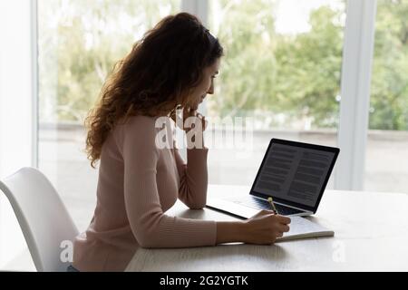 Hispanic woman sit at desk work study on laptop Stock Photo