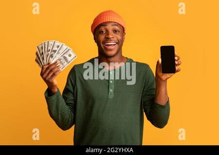 Cheerful Young Black Man Holding Smartphone With Blank Screen And Holding Cash Stock Photo