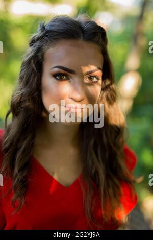 A portrait of an attractive Caucasian female wearing a vibrant red dress on background of trees Stock Photo