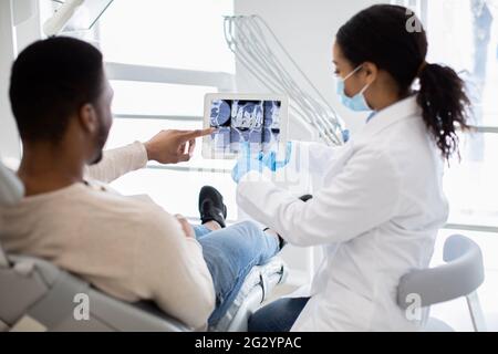 Female dentist showing xray of teeth treatment on digital tablet to patient Stock Photo