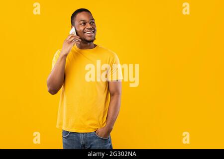 Happy African American Guy Talking On Phone Over Yellow Background Stock Photo