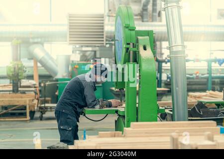 Worker at grinding machine for processing wood in workshop of woodworking plant. Stock Photo