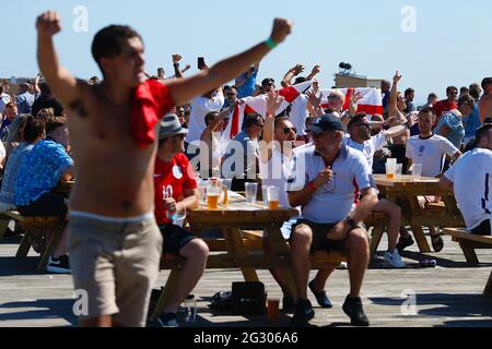 Hastings, East Sussex, UK. 13 June, 2021. England fans drink outside in the sunny weather on the Hastings pier fan zone that has provided a large screen and beer bar. Jubilant England fans celebrate the first goal. Photo Credit: Paul Lawrenson /Alamy Live News Stock Photo