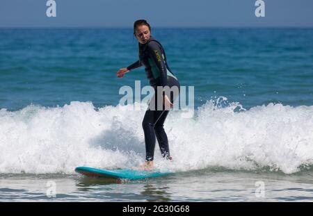 Harlyn Bay, Cornwall, UK. Sunday 13th June 2021, UK Weather:  The hottest day of the year so far with many people hitting the beach to call off in the sea.  A female surfer hitting the waves on the hottest day of the year so far at Harlyn Bay, Cornwall  © DGDImages/Alamy Live News Stock Photo