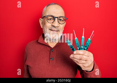 Handsome mature man holding picklock to unlock security door looking positive and happy standing and smiling with a confident smile showing teeth Stock Photo
