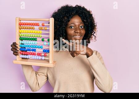 Young african american woman holding traditional abacus smiling happy pointing with hand and finger Stock Photo