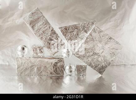 Geometric composition of several three-dimensional shapes covered with metal foil on a foil background. Stock Photo