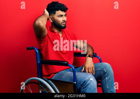 Arab man with beard sitting on wheelchair confuse and wondering about question. uncertain with doubt, thinking with hand on head. pensive concept. Stock Photo