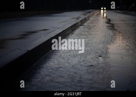 Car headlights in the distance. Road on a rainy day. A puddle on the highway. Lonely car lights on the road. Stock Photo