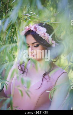 A portrait of an attractive Caucasian female wearing a floral headband seen through tree leaves Stock Photo