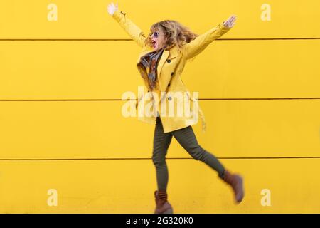 woman jumping on the street with yellow wall background Stock Photo