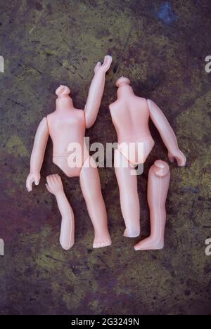 Two bodies of modern plastic dolls without heads and with some limbs detached lying on tarnished brass Stock Photo