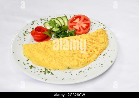 Tasty plain omelet in a plate, next to tomato cucumber and parsley, isolated on white background Stock Photo