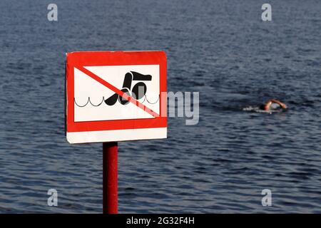 No swimming sign on background of sea and swimmer. Beach holiday on summer sea or river Stock Photo