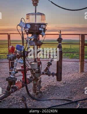 detail of oil well head with pump-jack, silhouette against sunrise sky and green prairie of Pawnee National Grassland in COlorado Stock Photo