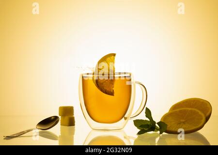 Cup of tea and glass teapot on glass with orange background. Stock Photo