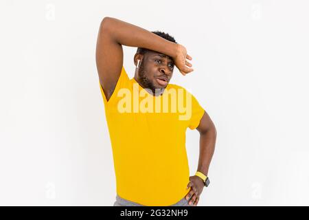 Tired afro american sporty man in bright yellow sportswear feeling exhausted after workout exercising at home using modern gadgets over white Stock Photo