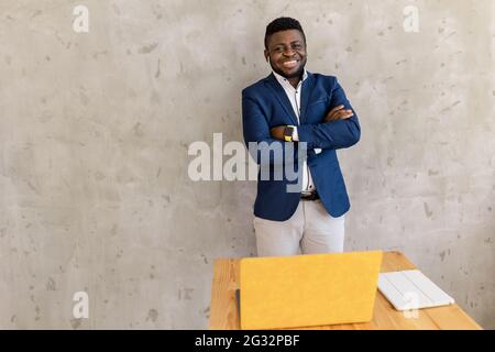 Portrait of smart afro american man businessman leader staying near desk and yellow laptop, smiling and cross hands ready decide solution wear suit Stock Photo