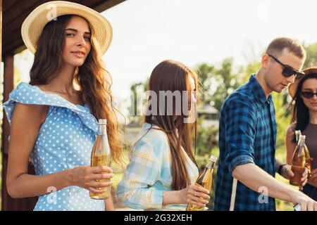 Young friends have fun, drink drinks, happy people together make barbecue vegetables and meat on the grill, on a picnic in nature, outdoors Stock Photo