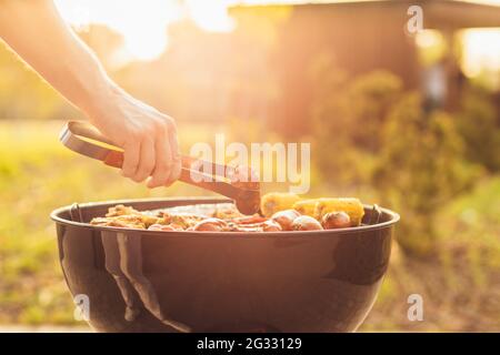 Assortment of fresh healthy vegetables, meat and sausages grilled on a hot fire on a charcoal grill, in a green grassy spring or summer field with cop Stock Photo