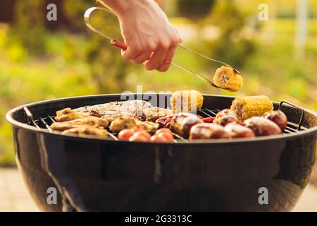Assortment of fresh healthy vegetables, meat and sausages grilled on a hot fire on a charcoal grill, in a green grassy spring or summer field with cop Stock Photo