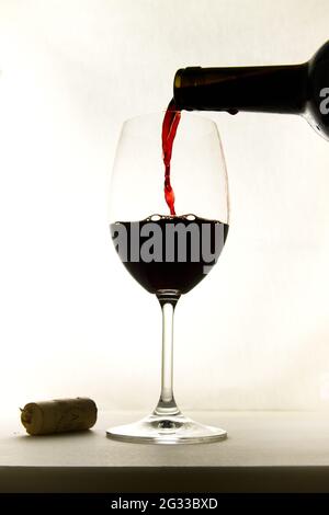 Silhouette of a wine glass in which they are putting red wine from the bottle directly, the background is white and the glass is isolated Stock Photo