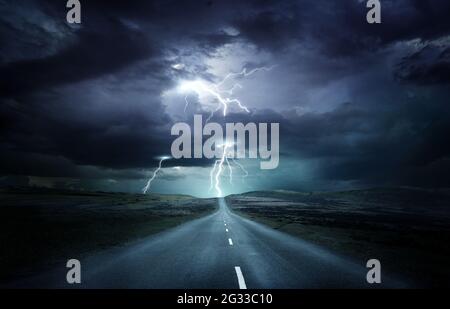 Extreme weather conditions. An empty landscape with a road leading into a powerful thunderstorm with lightning strikes. Photo composition. Stock Photo