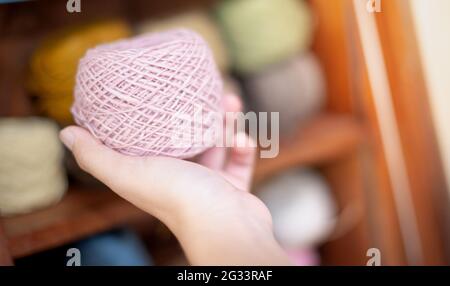 Female hand holding the pink yarn ball with the earth tone yarn in the wooden cupboard prepare for made Crochet and knitting. For leisure concept. Stock Photo
