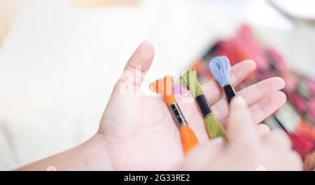 Close up hands of tailor woman holding many threads of different colors on table and prepare to use with white cotton and frame wood. For hobby. Stock Photo