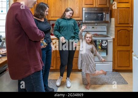 Four year old niece acting silly for her aunt, uncle and cousin, in a kitchen. (MR) Stock Photo