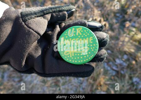 Gloved hand holding up kindness rock with encouraging UR Awesome message Stock Photo