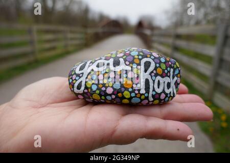 Kindness rock with painted you rock message and colorful polka dots held up on hand close-up Stock Photo