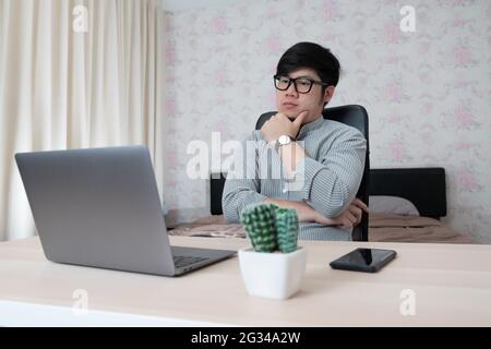 Young businessman in eyewear  working at home with laptop and phone on desk. Pleasant happy man communicating in social network, searching information Stock Photo