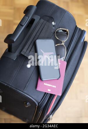 Vertical shot of face mask, passport, sunglasses, and phone with airplane wallpaper on black luggage
