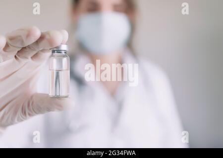 Doctor or nurse in protective face mask and gloves with stethoscope is holding glass vial bottle of anti virus vaccine. High quality photo Stock Photo