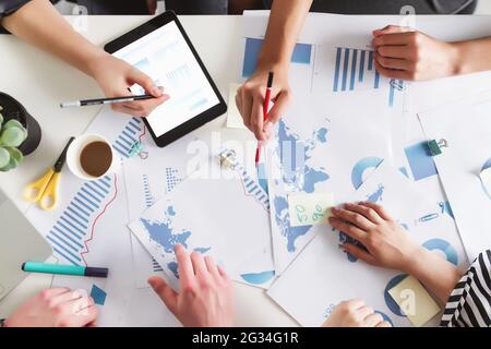Business planning process with colleagues or partners sitting together at the table with different graphics, charts, documents and tablet discussing a Stock Photo