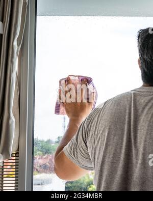 The concept of home apartment cleaning. A hand on the window and wipes with a rag. view from behind. Stock Photo